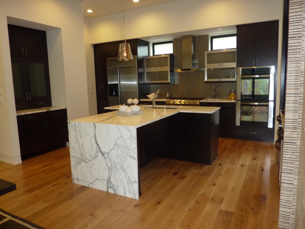 Example of a large minimalist single-wall medium tone wood floor and brown floor eat-in kitchen design in Portland with an undermount sink, flat-panel cabinets, dark wood cabinets, marble countertops, green backsplash, subway tile backsplash, stainless steel appliances and an island