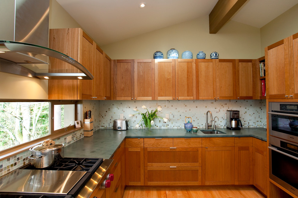 Mid-century modern u-shaped enclosed kitchen photo in Seattle with recessed-panel cabinets, medium tone wood cabinets, wood countertops, multicolored backsplash, mosaic tile backsplash and stainless steel appliances