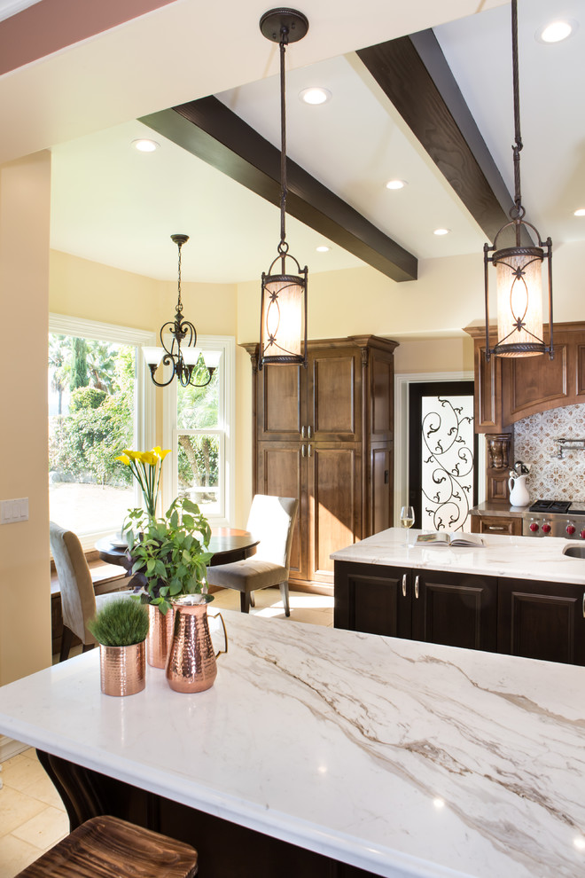 This is an example of an expansive mediterranean kitchen/diner in Los Angeles with a submerged sink, recessed-panel cabinets, dark wood cabinets, marble worktops, beige splashback, stone tiled splashback, stainless steel appliances, travertine flooring, multiple islands and beige floors.