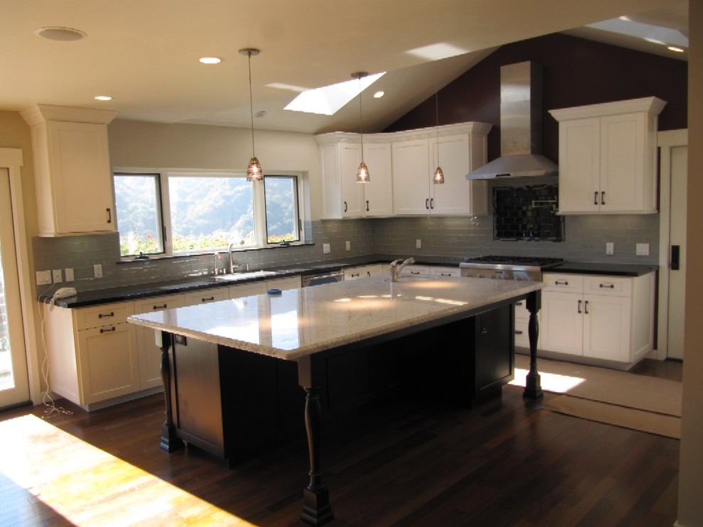 Elegant medium tone wood floor kitchen photo in Los Angeles with white cabinets, gray backsplash, stainless steel appliances and an island
