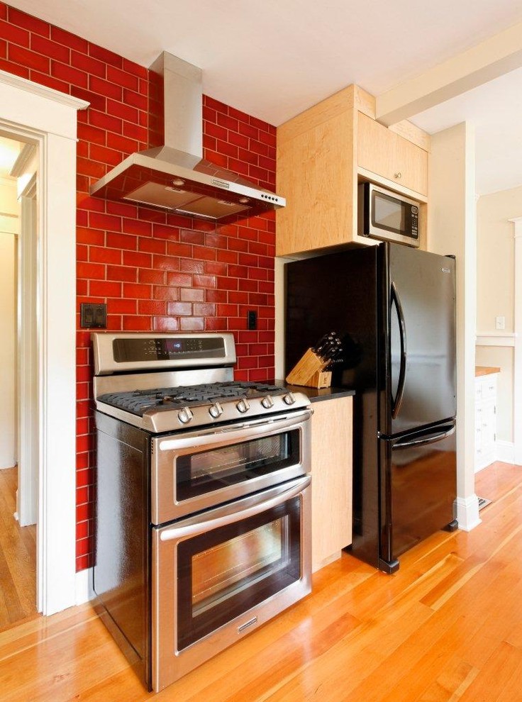 Immagine di una cucina minimalista con elettrodomestici neri, top in granito, paraspruzzi con piastrelle in ceramica, ante lisce, ante in legno chiaro e paraspruzzi rosso