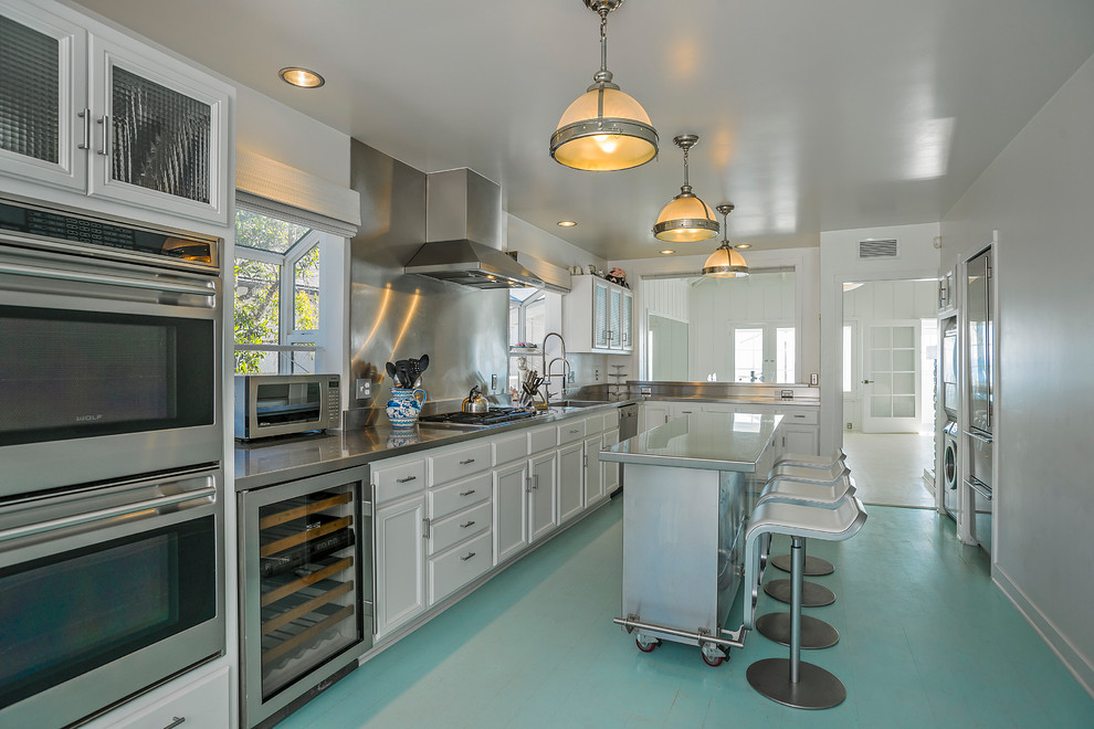 Enclosed kitchen - mid-sized coastal l-shaped painted wood floor enclosed kitchen idea in Santa Barbara with an undermount sink, recessed-panel cabinets, white cabinets, stainless steel countertops, metallic backsplash, stainless steel appliances and an island