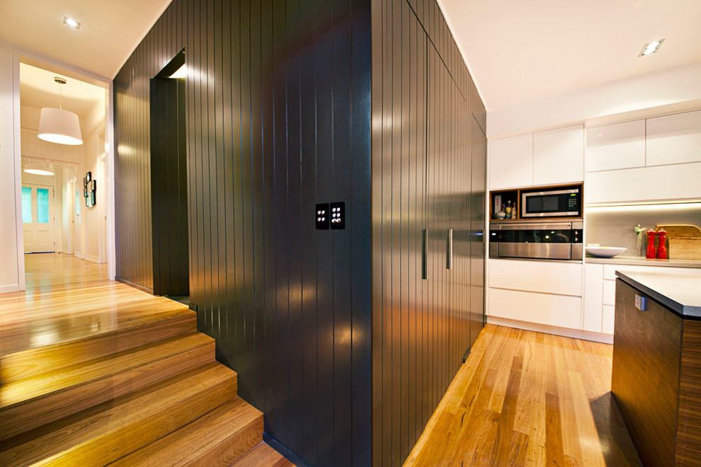Photo of a contemporary galley kitchen in Brisbane with a submerged sink, engineered stone countertops, grey splashback, stone slab splashback, stainless steel appliances, light hardwood flooring and an island.