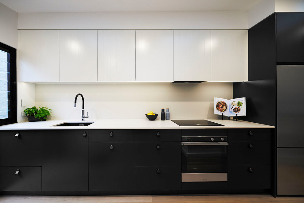 This is an example of a small modern single-wall kitchen/diner in Sydney with a submerged sink, flat-panel cabinets, black cabinets, engineered stone countertops, grey splashback, stone slab splashback, stainless steel appliances, light hardwood flooring, no island, brown floors and grey worktops.
