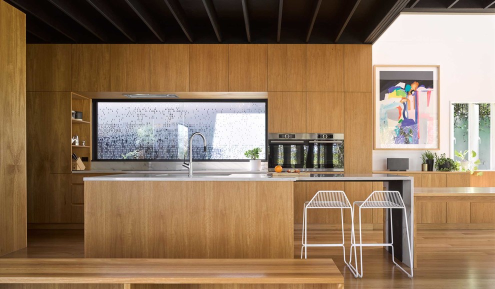 Источник вдохновения для домашнего уюта: параллельная кухня-гостиная в современном стиле с врезной мойкой, плоскими фасадами, фасадами цвета дерева среднего тона, фартуком из стекла, светлым паркетным полом и островом