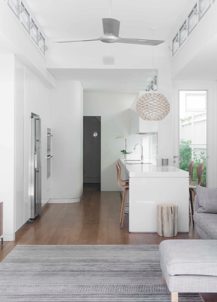Ejemplo de cocina contemporánea abierta con suelo de madera en tonos medios, electrodomésticos de acero inoxidable, puertas de armario blancas y armarios con paneles lisos
