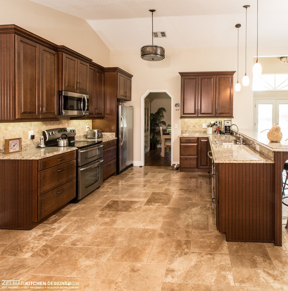 Bild på ett stort vintage kök, med en undermonterad diskho, luckor med upphöjd panel, bruna skåp, granitbänkskiva, beige stänkskydd, stänkskydd i stenkakel, rostfria vitvaror, travertin golv och en halv köksö