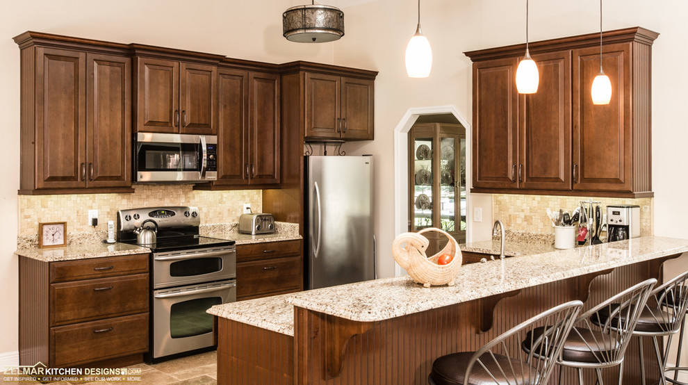 Inspiration for a large timeless u-shaped travertine floor open concept kitchen remodel in Orlando with an undermount sink, raised-panel cabinets, brown cabinets, granite countertops, beige backsplash, stone tile backsplash, stainless steel appliances and a peninsula