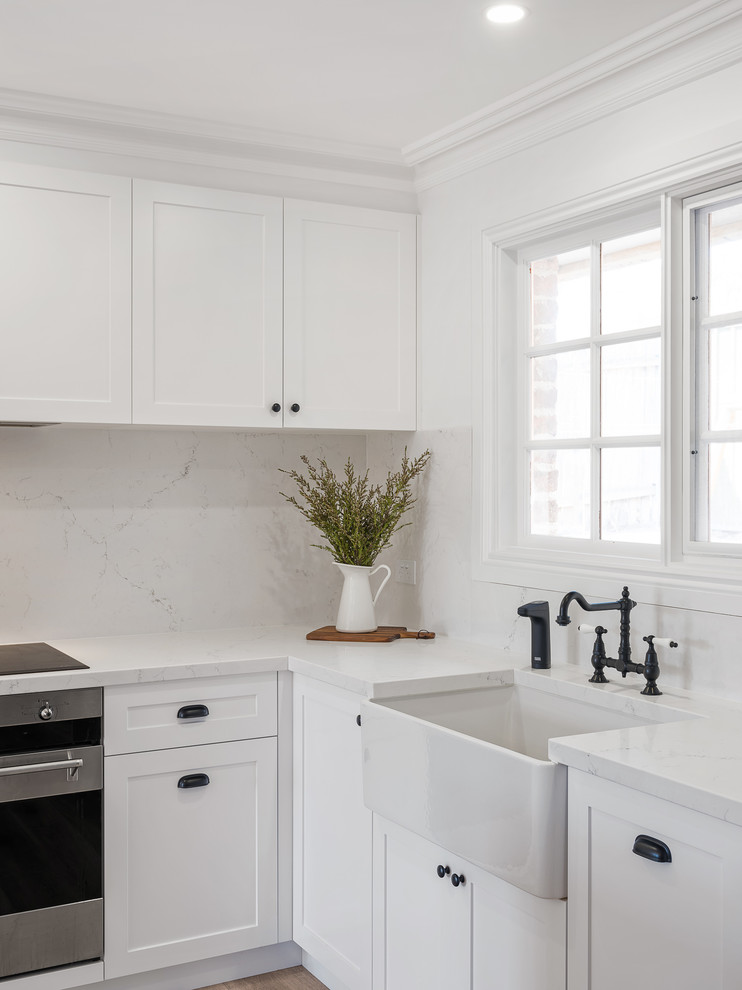 Idéer för att renovera ett mellanstort vintage vit vitt kök, med en rustik diskho, skåp i shakerstil, vita skåp, marmorbänkskiva, vitt stänkskydd, stänkskydd i marmor, rostfria vitvaror, laminatgolv, en köksö och brunt golv