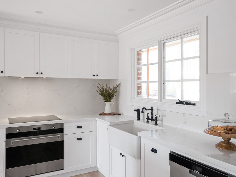 Foto på ett mellanstort vintage vit kök, med en rustik diskho, skåp i shakerstil, vita skåp, marmorbänkskiva, vitt stänkskydd, stänkskydd i marmor, rostfria vitvaror, laminatgolv, en köksö och brunt golv