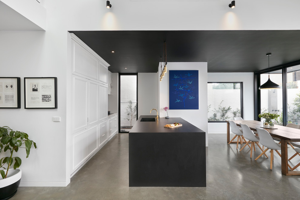 Offene, Zweizeilige Moderne Küche mit Unterbauwaschbecken, Schrankfronten mit vertiefter Füllung, weißen Schränken, Betonboden, Kücheninsel, grauem Boden und schwarzer Arbeitsplatte in Melbourne