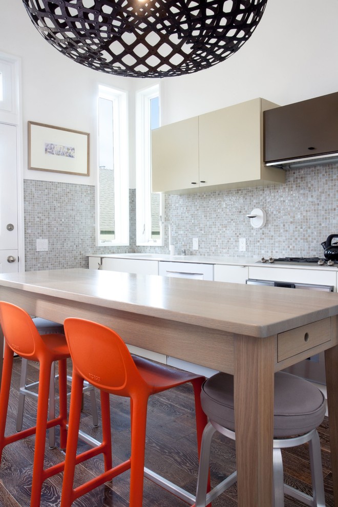 Example of a trendy galley medium tone wood floor and brown floor eat-in kitchen design in San Francisco with flat-panel cabinets, beige cabinets, wood countertops, gray backsplash, mosaic tile backsplash, stainless steel appliances, an island and brown countertops