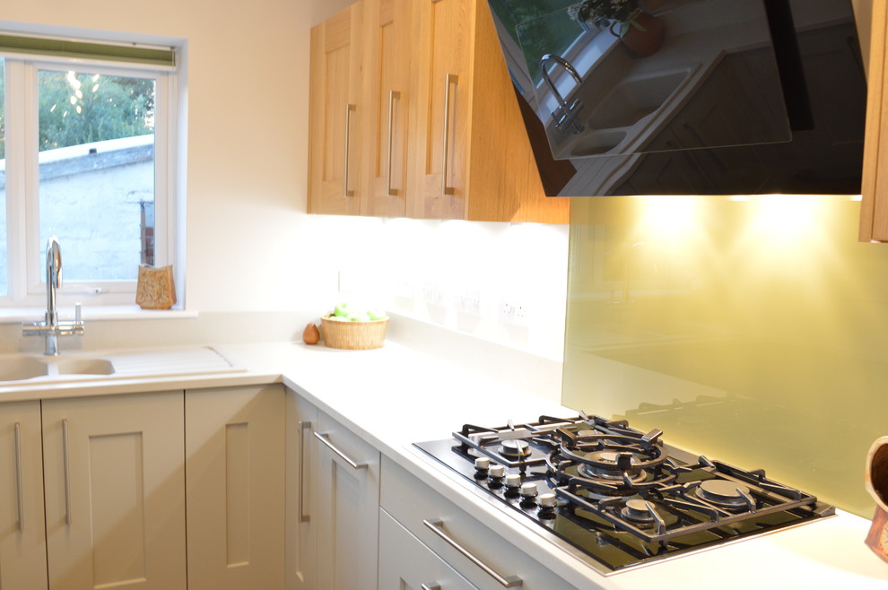 Imagen de cocina tradicional pequeña con armarios estilo shaker, encimera de acrílico, salpicadero gris, salpicadero de vidrio templado y electrodomésticos de acero inoxidable
