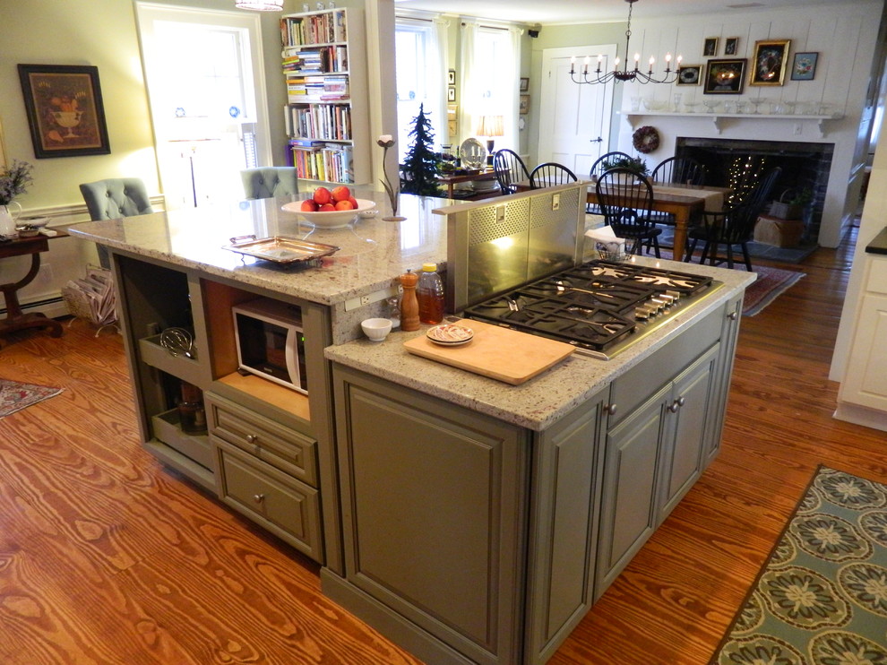 Modelo de cocina clásica, de tamaño medio, con fregadero de un seno, armarios con paneles con relieve, puertas de armario blancas, encimera de cuarzo compacto, salpicadero blanco, suelo de madera en tonos medios y una isla