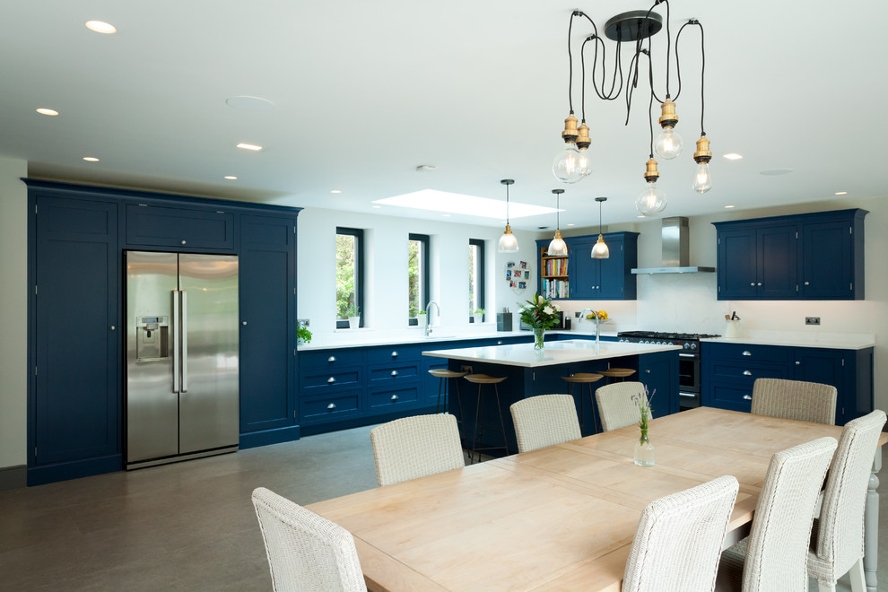 Inspiration for a large classic l-shaped kitchen/diner in Surrey with a double-bowl sink, shaker cabinets, blue cabinets, composite countertops, stainless steel appliances, limestone flooring, an island, beige floors and white worktops.