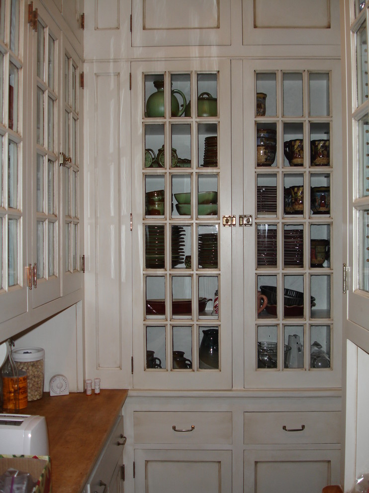 This is an example of a traditional galley kitchen pantry in Milwaukee with beaded cabinets, white cabinets, wood worktops, integrated appliances and travertine flooring.