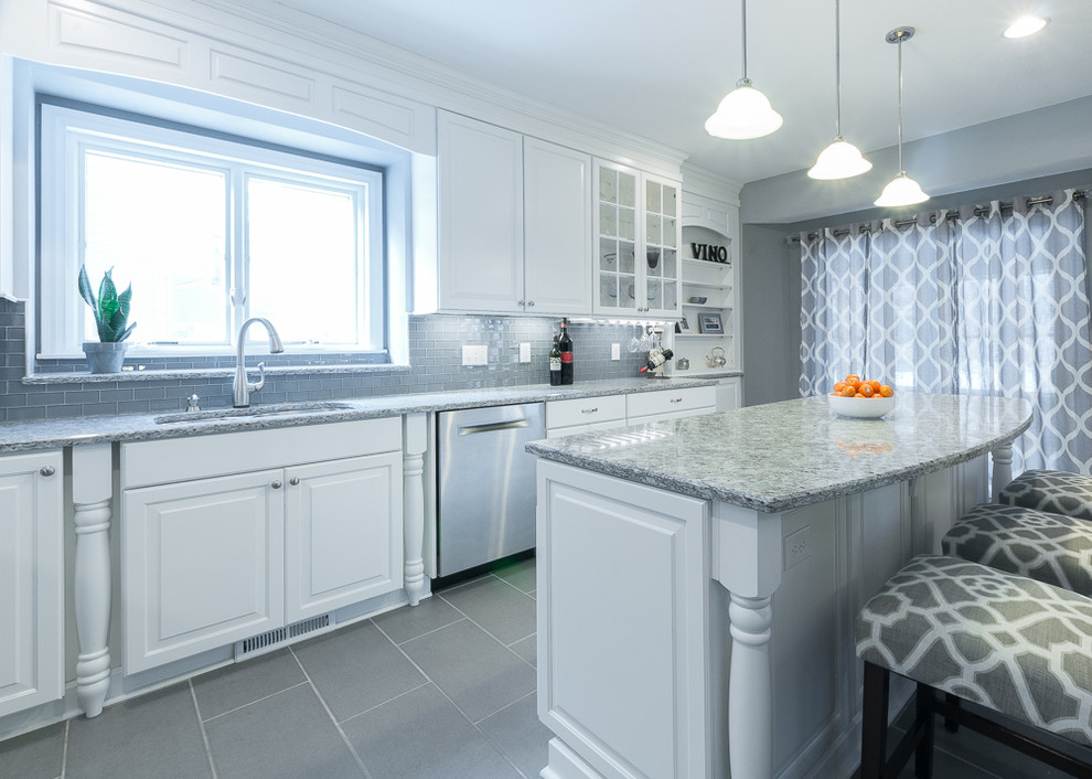 Eat-in kitchen - mid-sized traditional l-shaped porcelain tile eat-in kitchen idea in Minneapolis with an undermount sink, raised-panel cabinets, white cabinets, granite countertops, gray backsplash, glass tile backsplash, stainless steel appliances and an island