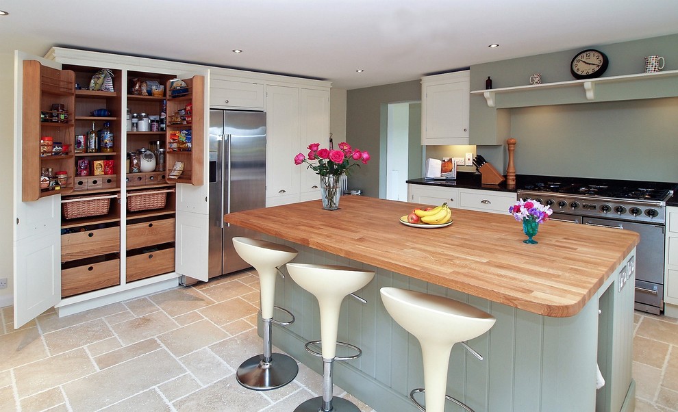 This is an example of a large traditional u-shaped enclosed kitchen in Hampshire with shaker cabinets, green cabinets, wood worktops, grey splashback, glass sheet splashback, stainless steel appliances, limestone flooring, an island, beige floors and brown worktops.