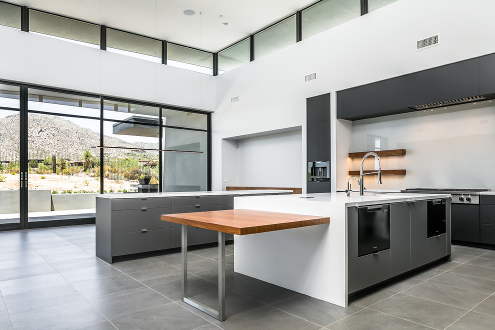 Design ideas for an expansive contemporary l-shaped open plan kitchen in Phoenix with a submerged sink, flat-panel cabinets, grey cabinets, engineered stone countertops, white splashback, glass sheet splashback, integrated appliances, porcelain flooring, multiple islands, grey floors and white worktops.