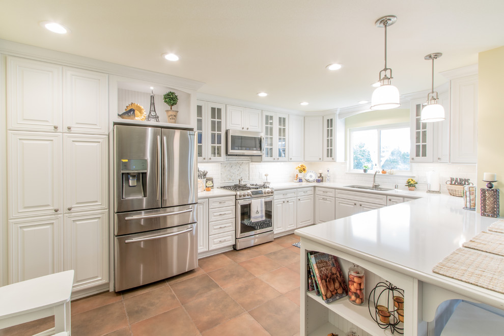 This is an example of a medium sized shabby-chic style u-shaped kitchen/diner in Orange County with a submerged sink, raised-panel cabinets, white cabinets, engineered stone countertops, white splashback, ceramic splashback, stainless steel appliances and porcelain flooring.