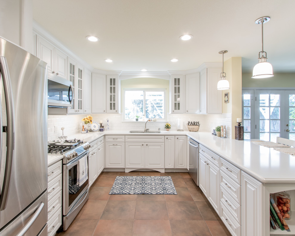 Photo of a medium sized traditional u-shaped kitchen/diner in Orange County with a submerged sink, raised-panel cabinets, white cabinets, engineered stone countertops, white splashback, ceramic splashback, stainless steel appliances, porcelain flooring and a breakfast bar.