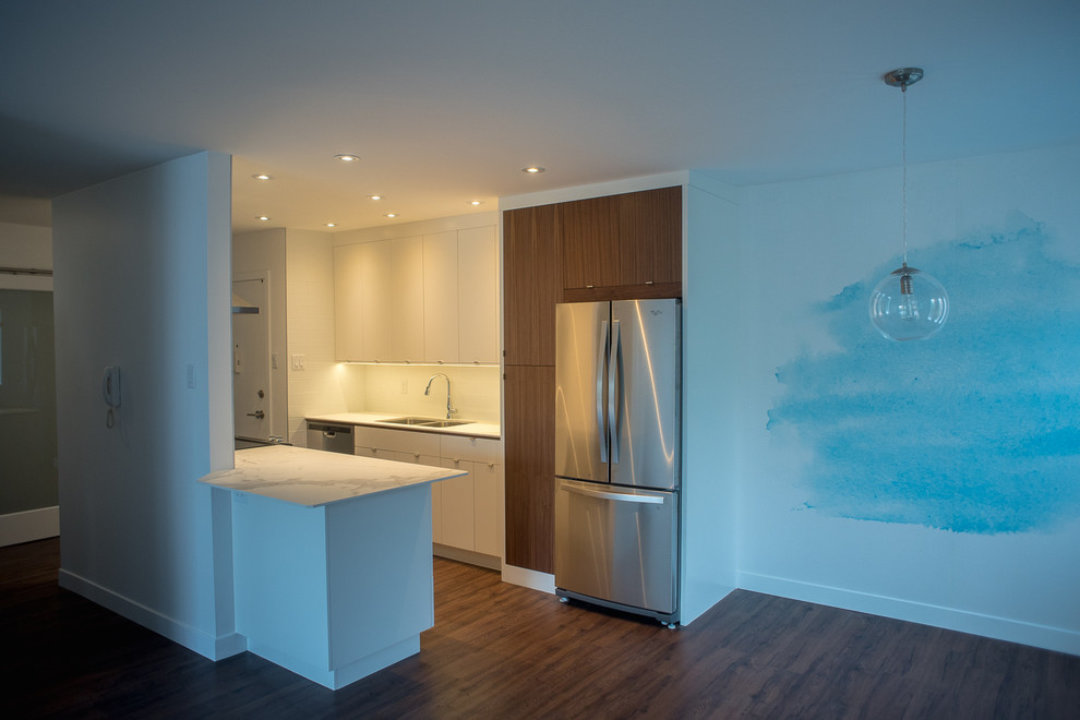 Small modern galley kitchen/diner in Vancouver with a submerged sink, flat-panel cabinets, white cabinets, composite countertops, white splashback, metro tiled splashback, stainless steel appliances and medium hardwood flooring.
