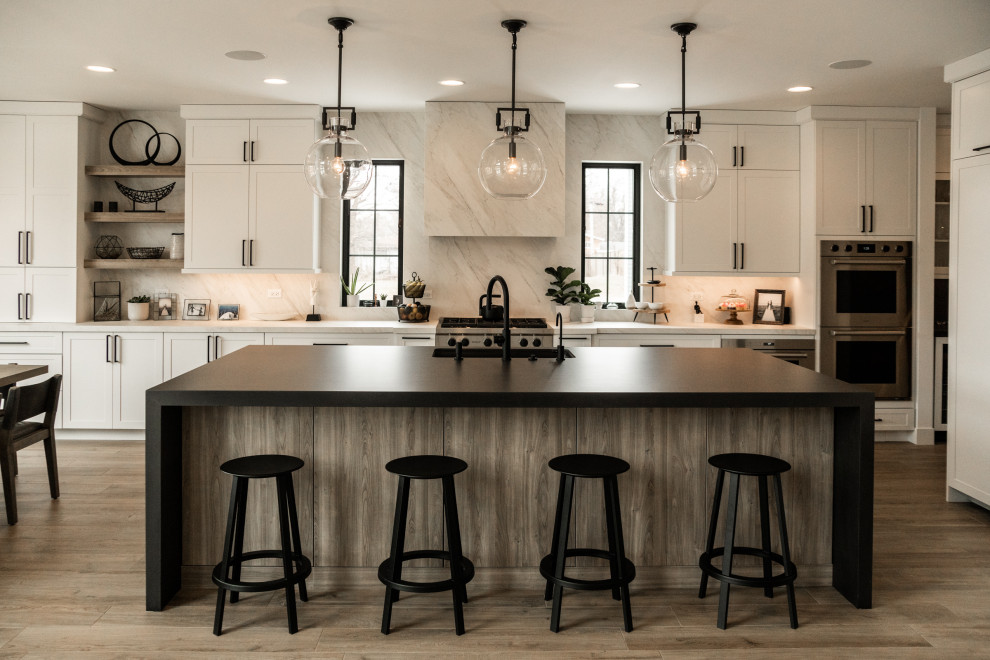 Design ideas for a traditional l-shaped kitchen/diner in Chicago with a submerged sink, shaker cabinets, white cabinets, white splashback, stone slab splashback, stainless steel appliances, medium hardwood flooring, an island, brown floors and white worktops.