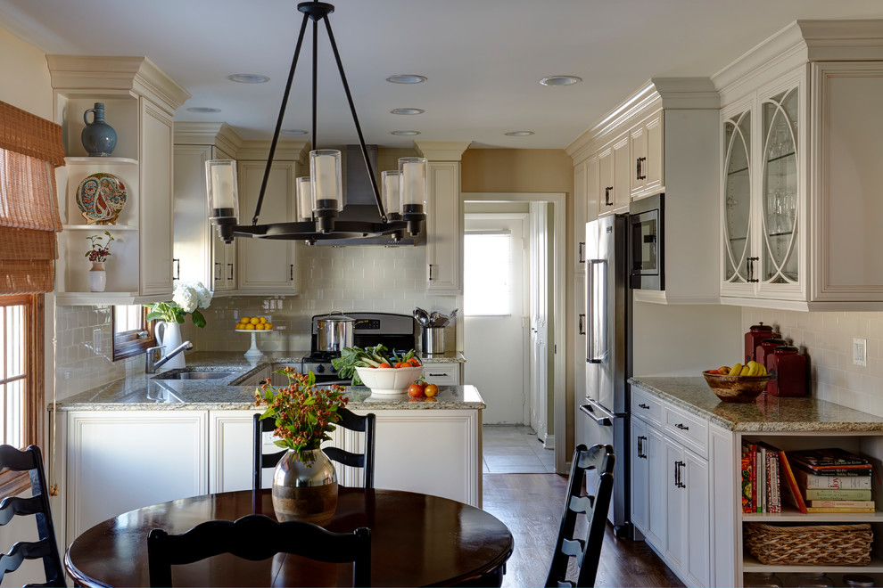 Bild på ett mellanstort lantligt u-kök, med en undermonterad diskho, luckor med infälld panel, vita skåp, granitbänkskiva, vitt stänkskydd, stänkskydd i tunnelbanekakel, rostfria vitvaror, mellanmörkt trägolv, en halv köksö och brunt golv