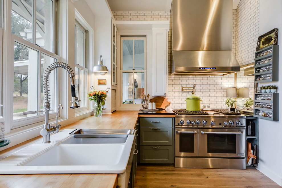 Example of a cottage light wood floor kitchen design in Austin with a farmhouse sink, shaker cabinets, green cabinets, wood countertops, white backsplash, subway tile backsplash and stainless steel appliances