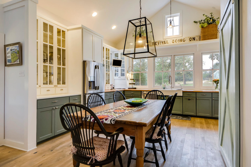 Inspiration for a rural u-shaped kitchen/diner in Austin with a belfast sink, green cabinets, wood worktops, stainless steel appliances, light hardwood flooring and shaker cabinets.
