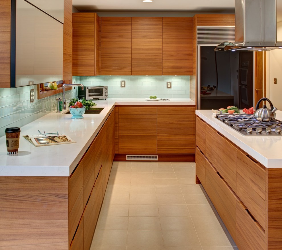 На фото: угловая кухня в современном стиле с двойной мойкой, плоскими фасадами, фасадами цвета дерева среднего тона, зеленым фартуком, фартуком из стеклянной плитки, черной техникой и островом