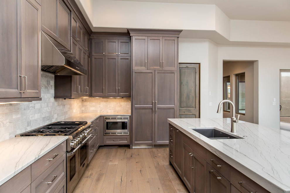 Inspiration for a large transitional l-shaped light wood floor and beige floor eat-in kitchen remodel in Las Vegas with a double-bowl sink, shaker cabinets, dark wood cabinets, marble countertops, gray backsplash, stone tile backsplash, stainless steel appliances and an island