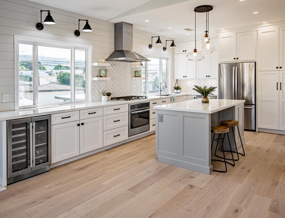 Inspiration for a farmhouse l-shaped medium tone wood floor and brown floor kitchen remodel in Orange County with an undermount sink, shaker cabinets, white cabinets, white backsplash, stainless steel appliances, an island and white countertops