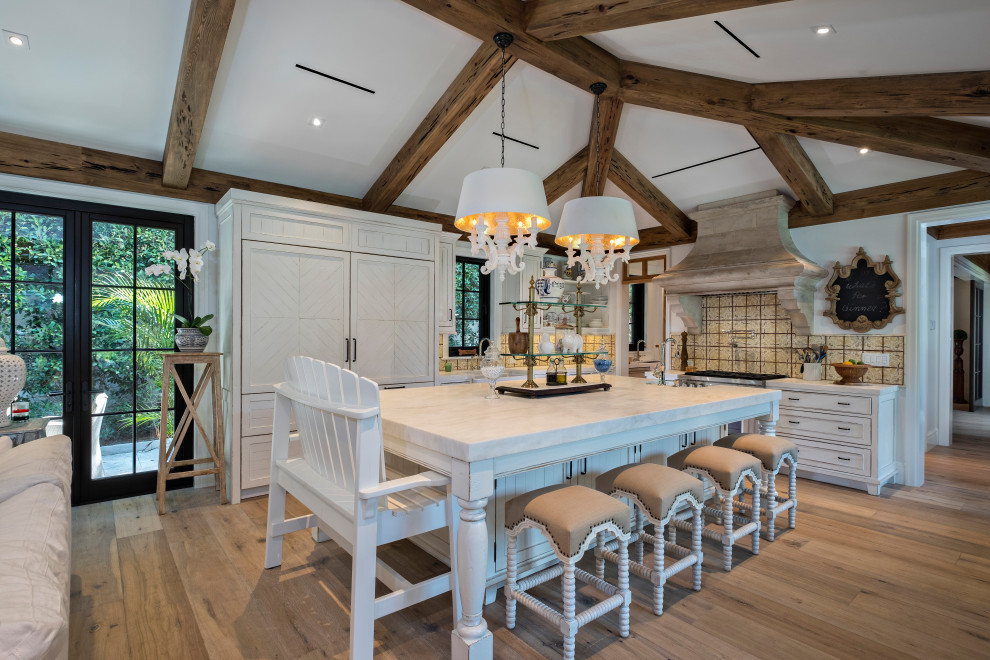 Example of a mid-sized beach style l-shaped light wood floor, brown floor and vaulted ceiling open concept kitchen design in Miami with white cabinets, marble countertops, multicolored backsplash, porcelain backsplash, stainless steel appliances, an island and white countertops