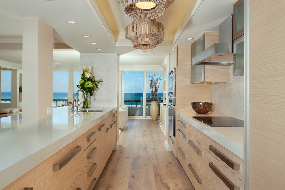 Example of a mid-sized trendy galley medium tone wood floor and brown floor open concept kitchen design in Miami with an undermount sink, flat-panel cabinets, light wood cabinets, marble countertops, beige backsplash, travertine backsplash, stainless steel appliances, no island and beige countertops
