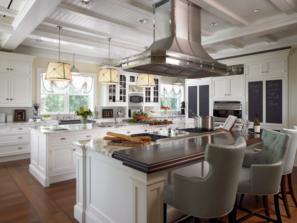 Klassisk inredning av ett kök, med en rustik diskho, skåp i shakerstil, vita skåp, grått stänkskydd, rostfria vitvaror, mellanmörkt trägolv och flera köksöar