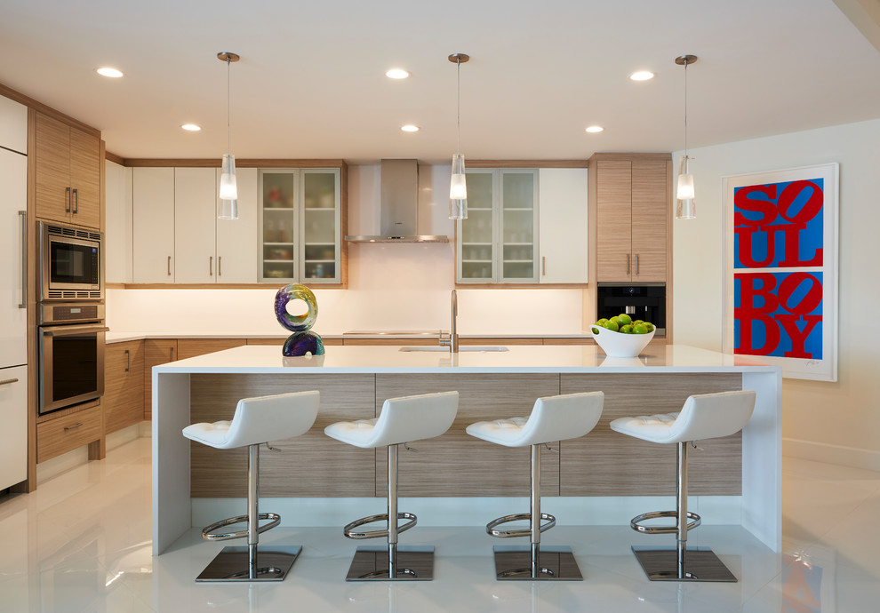 Стильный дизайн: угловая кухня в современном стиле с плоскими фасадами, светлыми деревянными фасадами, техникой из нержавеющей стали, островом и серым полом - последний тренд