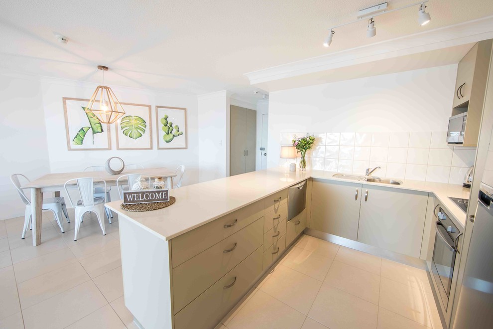 Design ideas for a small coastal u-shaped open plan kitchen in Gold Coast - Tweed with a single-bowl sink, flat-panel cabinets, beige cabinets, engineered stone countertops, white splashback, ceramic splashback, stainless steel appliances, ceramic flooring, beige floors and beige worktops.