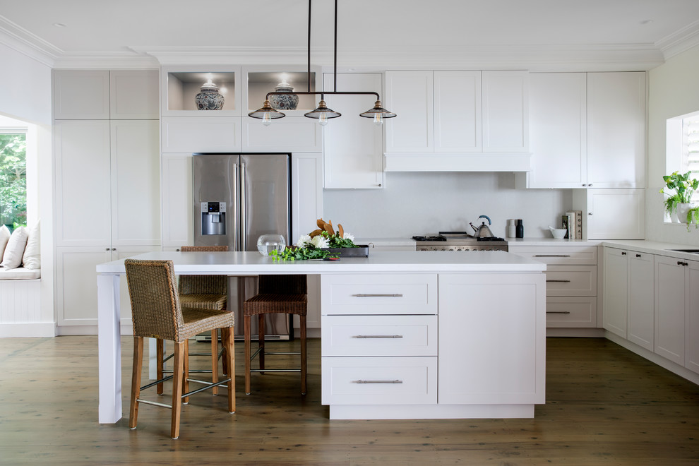 Klassische Küche in L-Form mit Unterbauwaschbecken, Schrankfronten im Shaker-Stil, weißen Schränken, Küchengeräten aus Edelstahl, braunem Holzboden, Kücheninsel, braunem Boden und weißer Arbeitsplatte in Sydney
