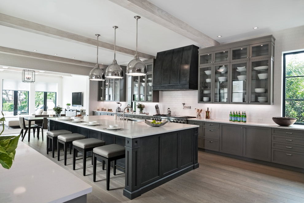 Inspiration for a traditional grey and black galley kitchen in Miami with a submerged sink, shaker cabinets, grey cabinets, white splashback, stainless steel appliances, medium hardwood flooring, an island, brown floors and white worktops.
