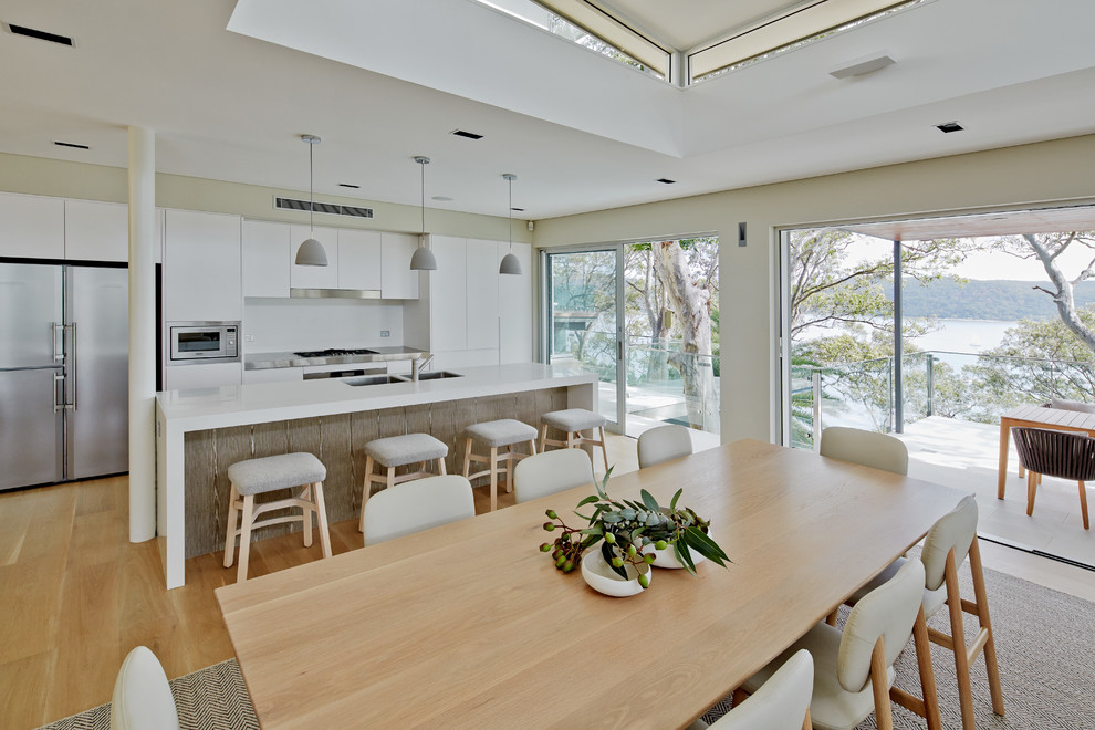 Diseño de cocina comedor escandinava con armarios con paneles lisos, puertas de armario blancas, electrodomésticos de acero inoxidable, suelo de madera en tonos medios y una isla