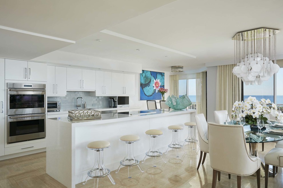 マイアミにあるビーチスタイルのおしゃれなキッチン (フラットパネル扉のキャビネット、白いキャビネット、グレーのキッチンパネル、シルバーの調理設備) の写真