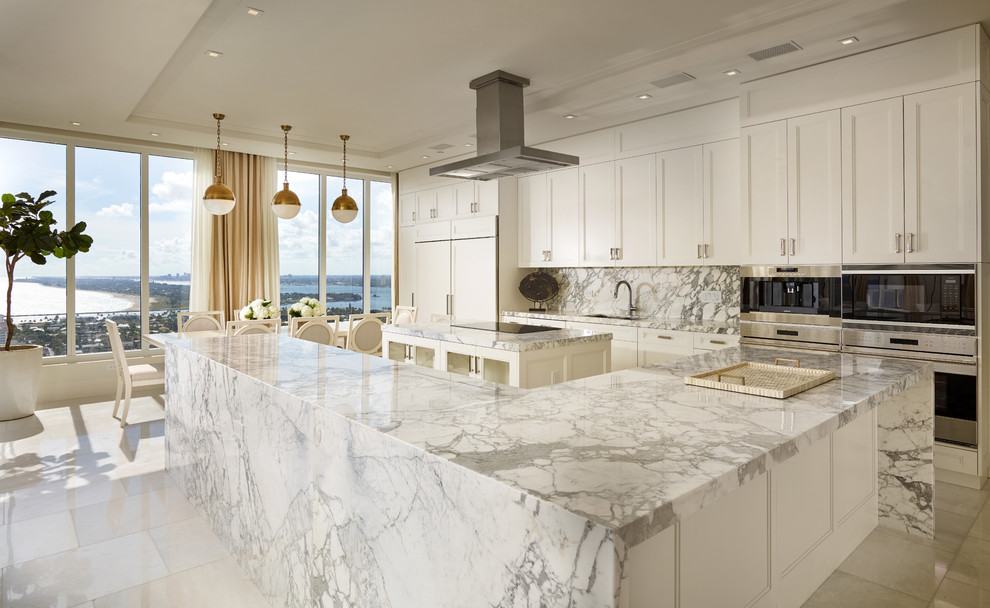 This is an example of a large classic kitchen/diner in Miami with a submerged sink, recessed-panel cabinets, white cabinets, marble worktops, white splashback, stone slab splashback, integrated appliances, marble flooring and multiple islands.