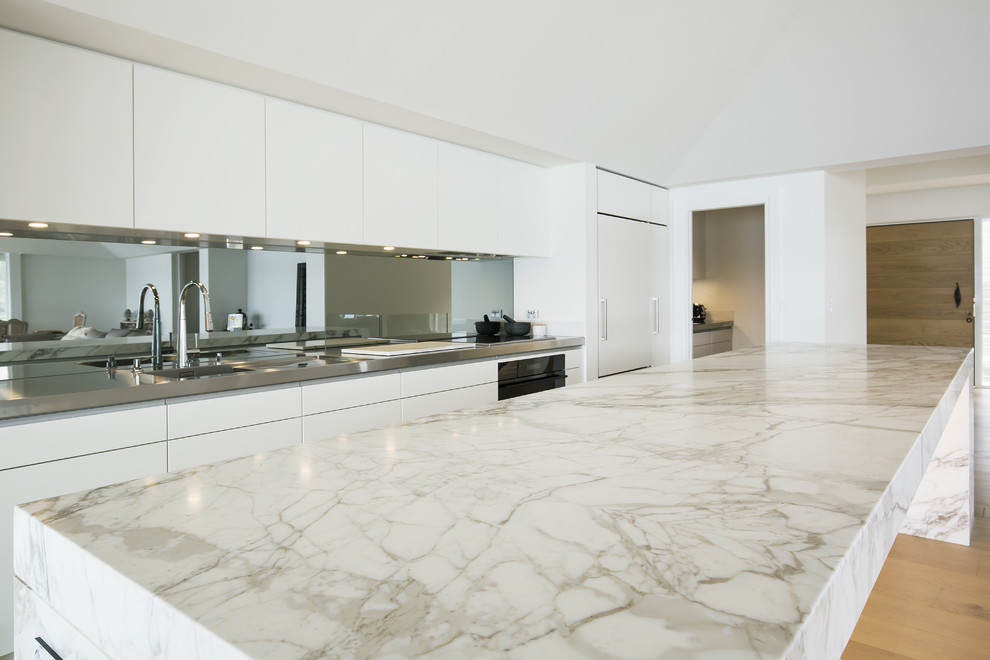Inspiration for a large modern single-wall light wood floor open concept kitchen remodel in Sydney with an integrated sink, flat-panel cabinets, beige cabinets, marble countertops, metallic backsplash, mirror backsplash, black appliances and an island