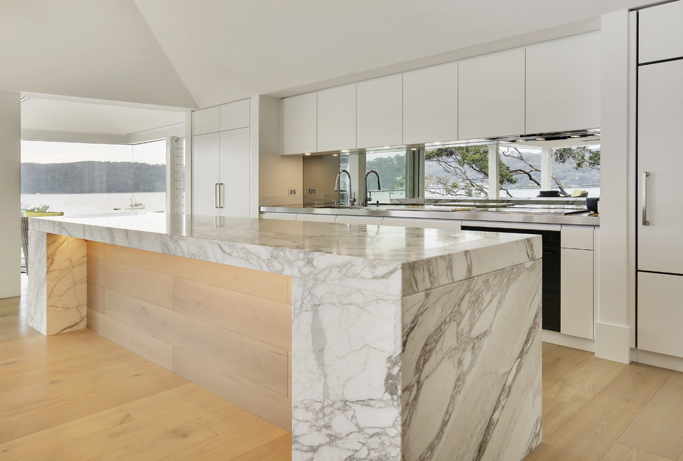 Esempio di una grande cucina minimalista con lavello integrato, ante lisce, ante beige, top in marmo, paraspruzzi a effetto metallico, paraspruzzi a specchio, elettrodomestici neri e parquet chiaro