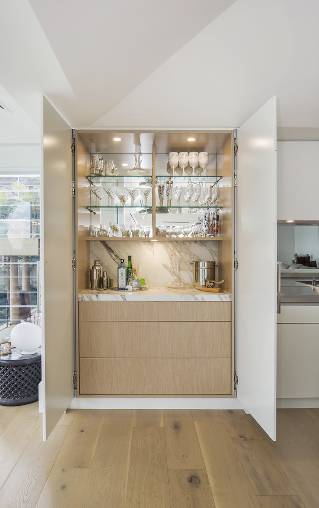 This is an example of a large modern single-wall open plan kitchen in Sydney with an integrated sink, flat-panel cabinets, beige cabinets, marble worktops, metallic splashback, mirror splashback, black appliances, light hardwood flooring and an island.