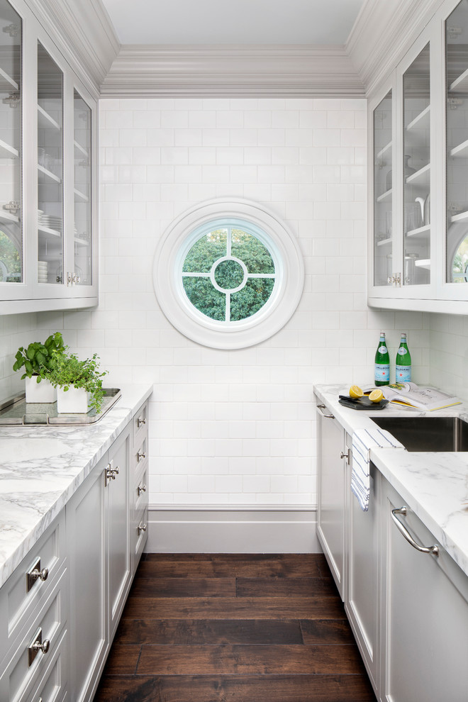 Exempel på ett maritimt flerfärgad flerfärgat kök, med en enkel diskho, luckor med glaspanel, grå skåp, marmorbänkskiva, vitt stänkskydd, stänkskydd i tunnelbanekakel, mörkt trägolv och brunt golv