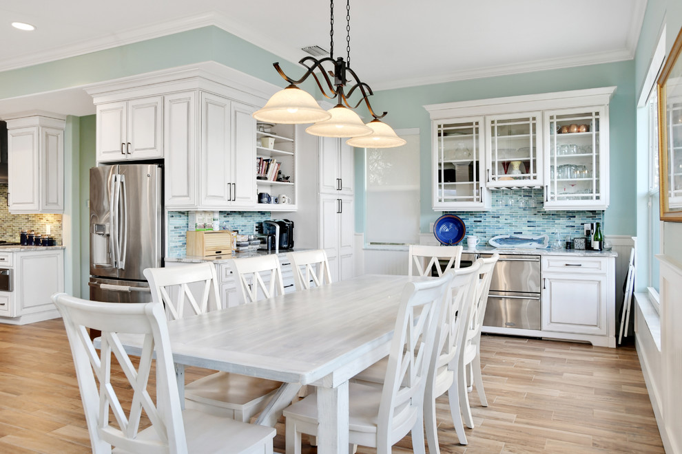 Inspiration for a large beach style l-shaped open plan kitchen in Tampa with a submerged sink, raised-panel cabinets, white cabinets, marble worktops, blue splashback, ceramic splashback, stainless steel appliances, light hardwood flooring, an island and brown floors.