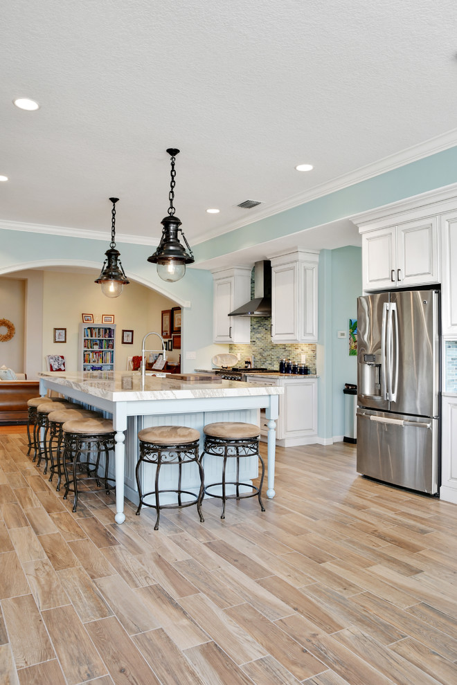 Inspiration for a large coastal l-shaped light wood floor and brown floor open concept kitchen remodel in Tampa with an undermount sink, raised-panel cabinets, white cabinets, marble countertops, blue backsplash, ceramic backsplash, stainless steel appliances and an island