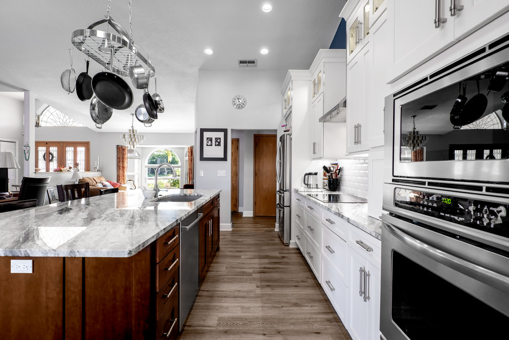 Inredning av ett klassiskt stort grå linjärt grått kök och matrum, med en enkel diskho, luckor med infälld panel, vita skåp, granitbänkskiva, vitt stänkskydd, stänkskydd i porslinskakel, rostfria vitvaror, vinylgolv, en köksö och brunt golv